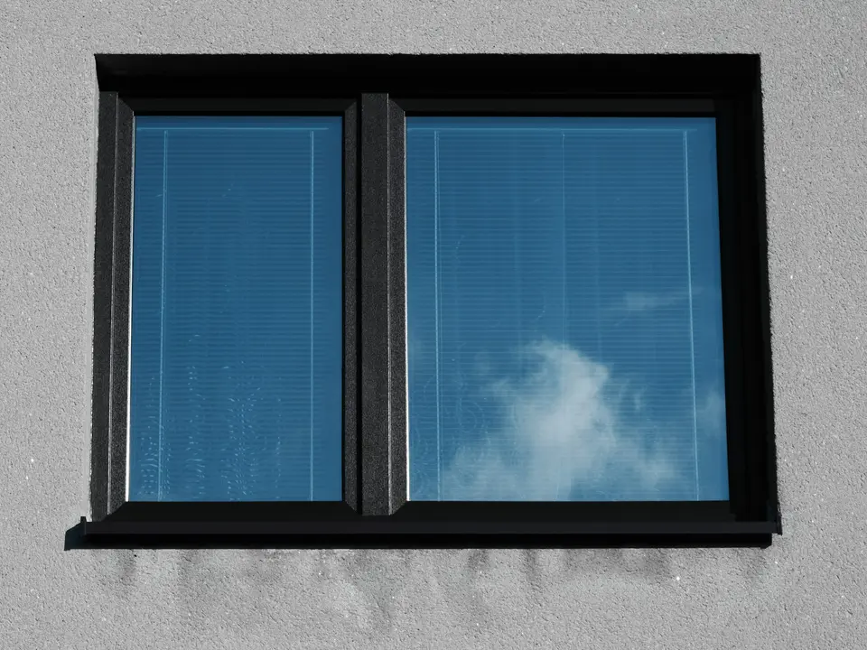 Een zwart kozijn met twee glasvlakken in een lichte gevel, met de lucht in het glas