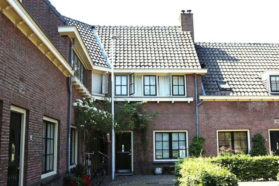 Bakstenen rijtjeshuizen rond een hofje met donkere en witte kozijnen, fietsen en rozen