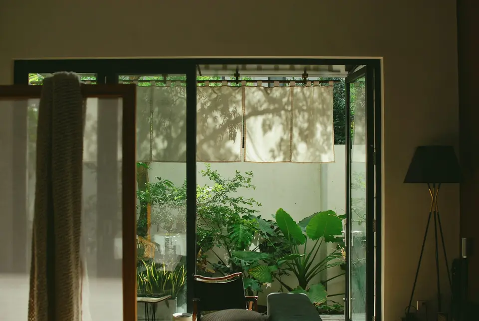Een open glazen pui in slanke donkere profielen naar een binnentuin vol planten
