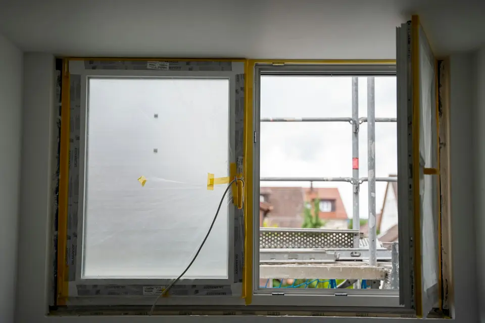 Een nieuw kozijn met afgeplakt glas in een raamopening, buiten staat een steiger